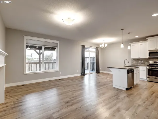 a view of an empty room and kitchen with wooden floor