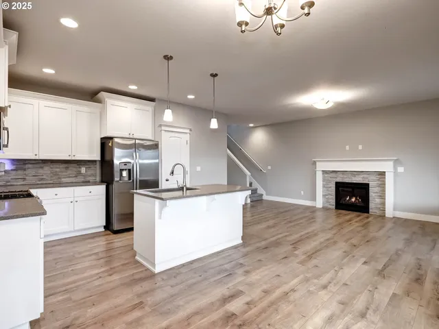 a large kitchen with kitchen island a stove a sink a refrigerator and white cabinets with wooden floor