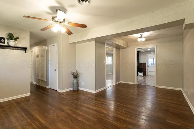a view of an empty room with wooden floor and a ceiling fan