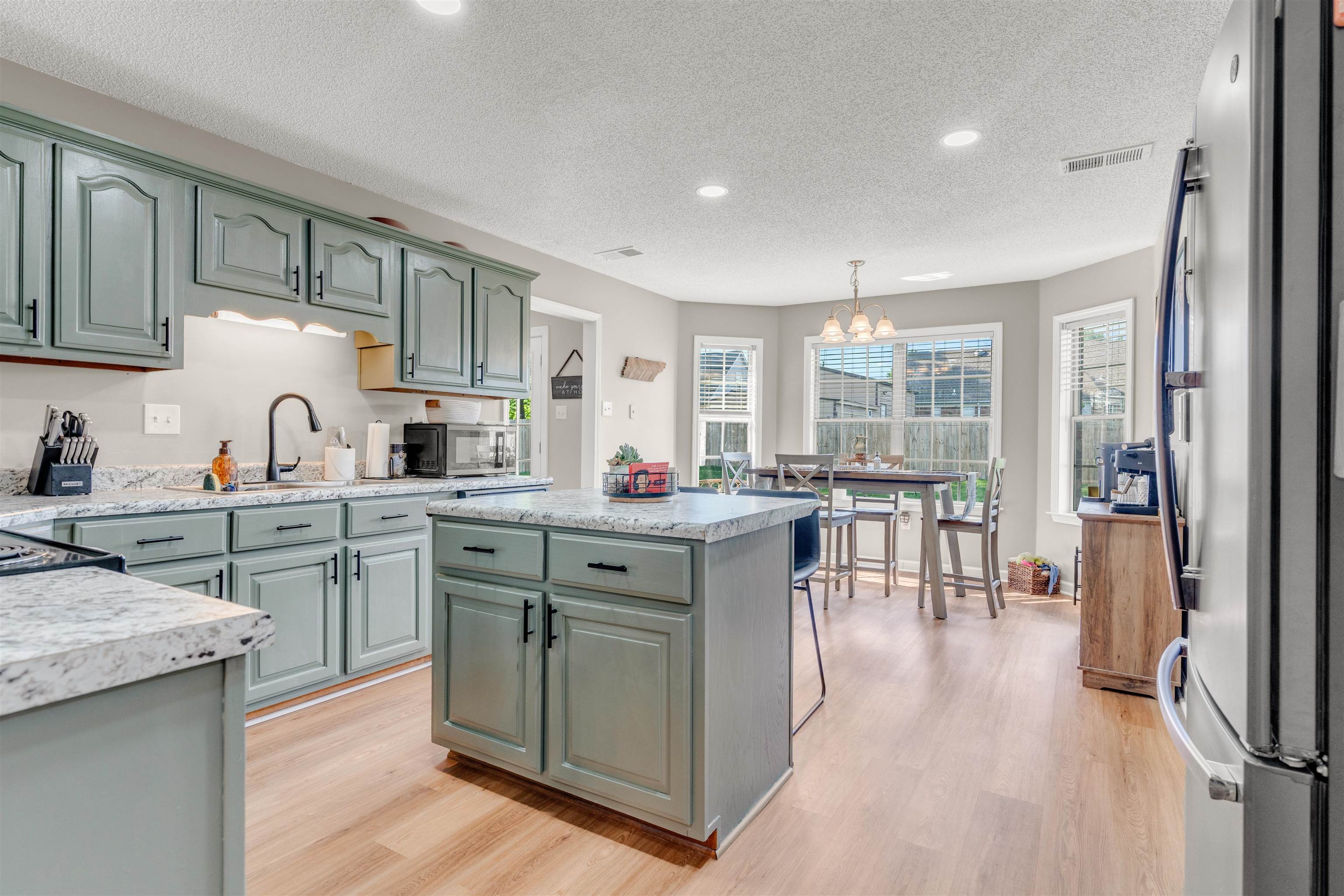 Kitchen featuring stainless steel appliances, light wood finished floors, light countertops, a textured ceiling, and a center island