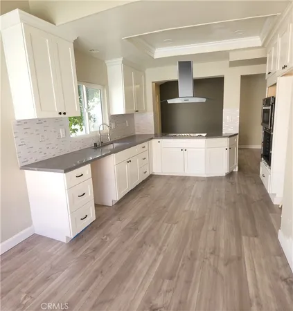 a large white kitchen with kitchen island wooden floors and stainless steel appliances