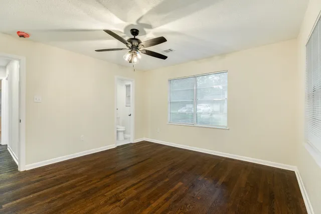 an empty room with wooden floor fan and windows
