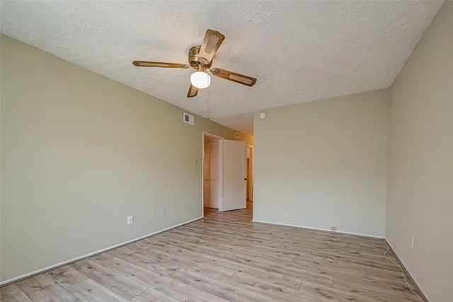an empty room with wooden floor chandelier fan and windows