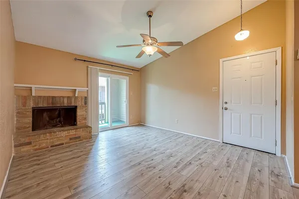 a view of an empty room with wooden floor fireplace and a window