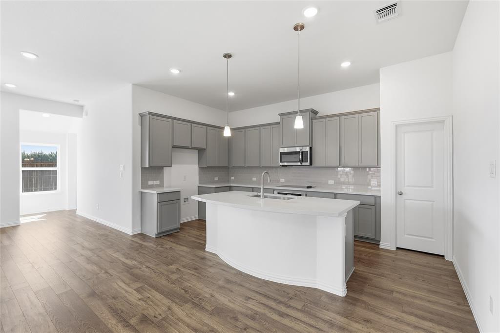 2529 Rivers W Road Anna, TX 75409 - Photo 16 of 40 Modern kitchen featuring light gray cabinetry, white countertops, a central island with sink, stainless steel microwave, and wood-finish flooring