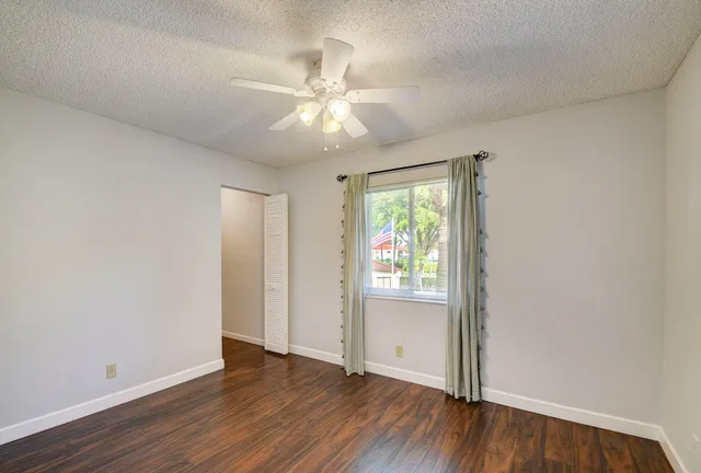 an empty room with wooden floor fan and windows