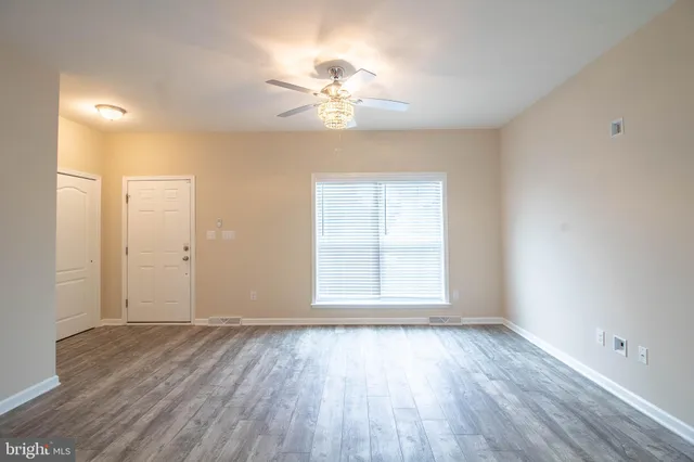 an empty room with wooden floor chandelier fan and windows