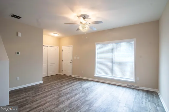 an empty room with wooden floor chandelier fan and windows
