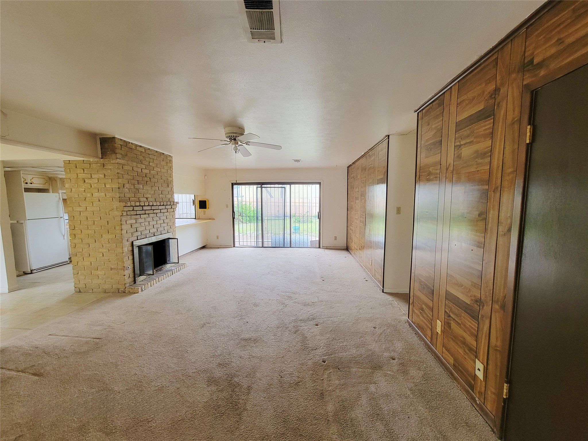 6605 Highpoint Drive Austin, TX 78723 - Photo 4 of 11 Open-concept living space featuring a brick fireplace, sliding glass door access to the exterior, wood-paneled accent walls, and a ceiling fan
