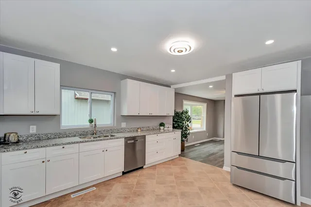 a kitchen with granite countertop a refrigerator a sink and white cabinets