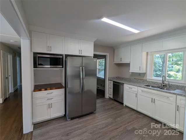 a kitchen with stainless steel appliances granite countertop a refrigerator a sink a stove and white cabinets with wooden floor