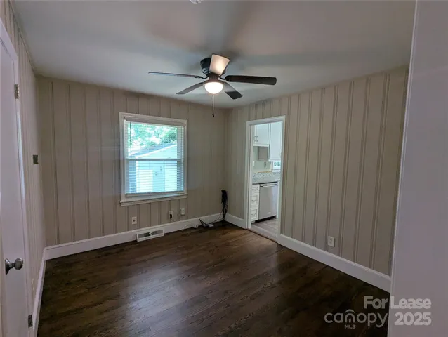 an empty room with wooden floor chandelier fan and windows