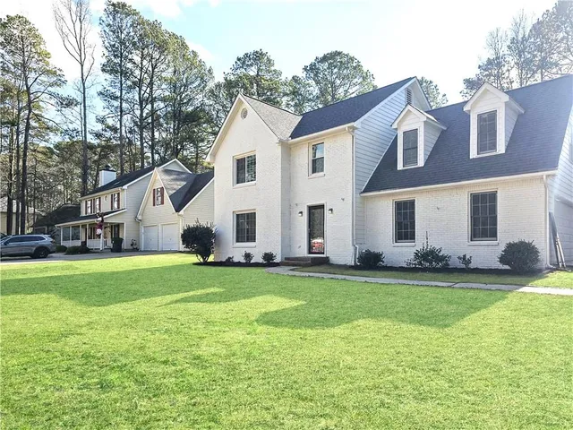 a view of a white house in front of a big yard with large trees