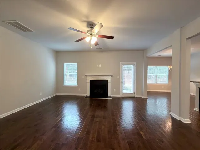 a view of an empty room with wooden floor and a kitchen