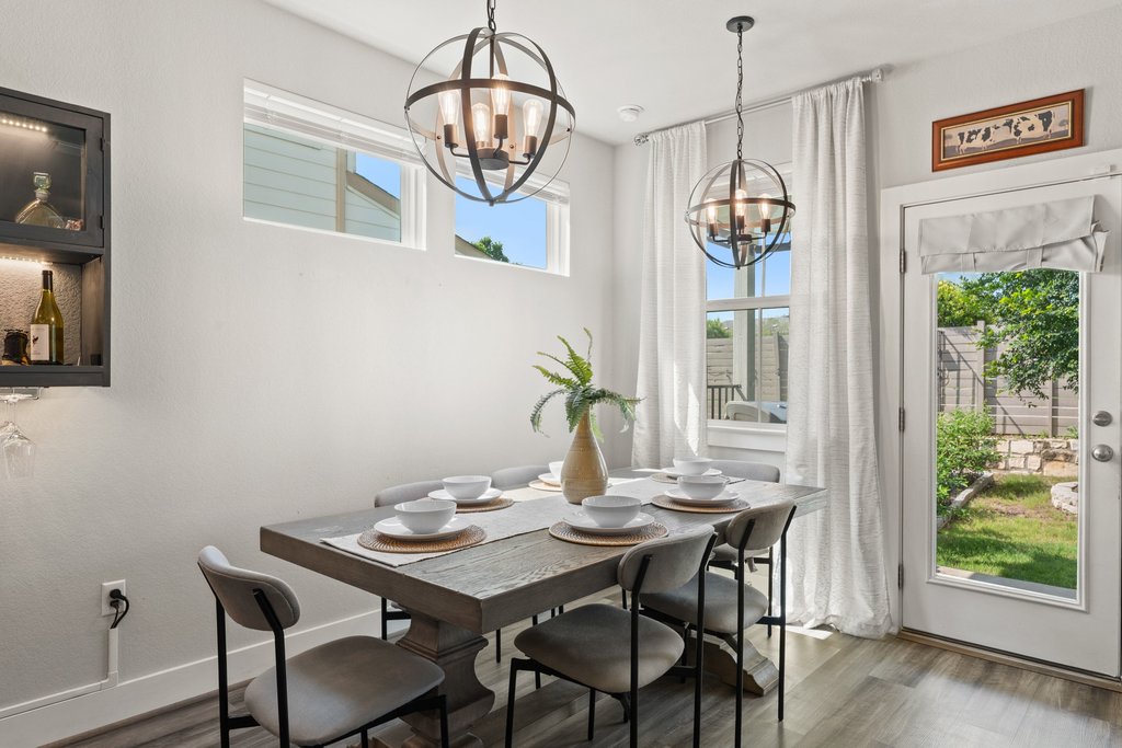 7403 Travertine Spring Drive, Unit 117 Austin, TX 78744 - Photo 4 of 37 Orb-shaped chandeliers illuminate this elegant dining area, boasting sleek wood flooring and a view of the garden.
