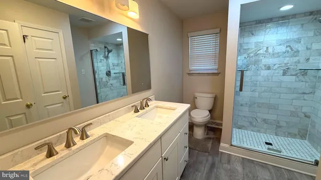 a bathroom with a granite countertop sink a toilet a mirror and shower