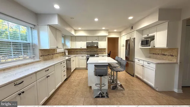 a kitchen with kitchen island granite countertop a sink cabinets stainless steel appliances and a large window