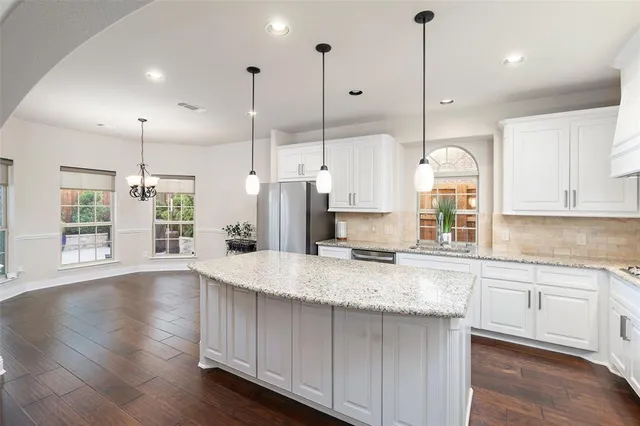 a kitchen with kitchen island granite countertop a stove a sink a center island a refrigerator and a wooden floor