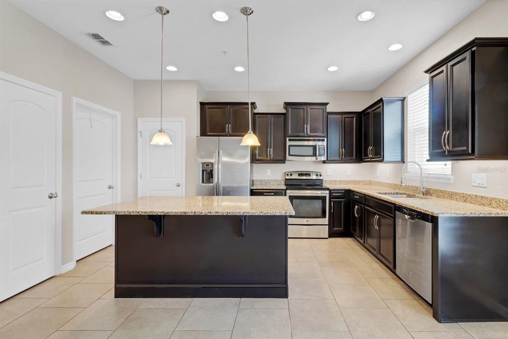 1578 Softshell Street St. Cloud, FL 34771 - Photo 9 of 27 a large kitchen with stainless steel appliances kitchen island granite countertop a stove top oven a sink dishwasher a dining table and chairs