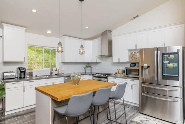 a kitchen with stainless steel appliances granite countertop a sink a stove a refrigerator and island with wooden floor