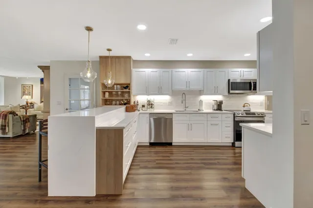 a kitchen with stainless steel appliances granite countertop a sink dishwasher a stove and white cabinets with wooden floor