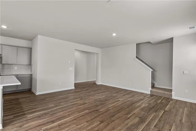 a view of an empty room with wooden floor and a kitchen