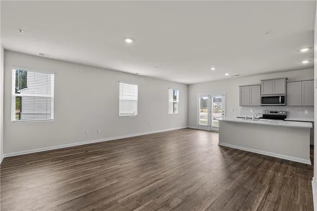 a kitchen with stainless steel appliances kitchen island granite countertop a stove top oven a sink a refrigerator and white cabinets with wooden floor