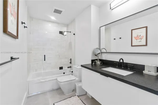 a bathroom with a granite countertop sink a toilet a mirror a bathtub and shower