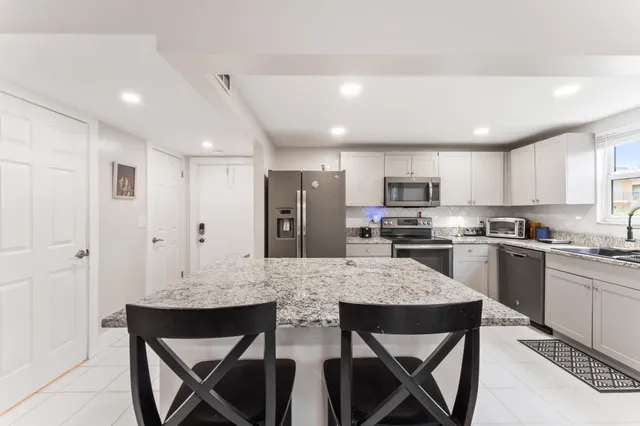 a large kitchen with kitchen island granite countertop a dining table chairs sink and refrigerator