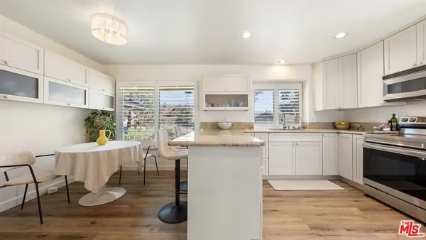 a kitchen with granite countertop a stove a sink and white cabinets with wooden floor