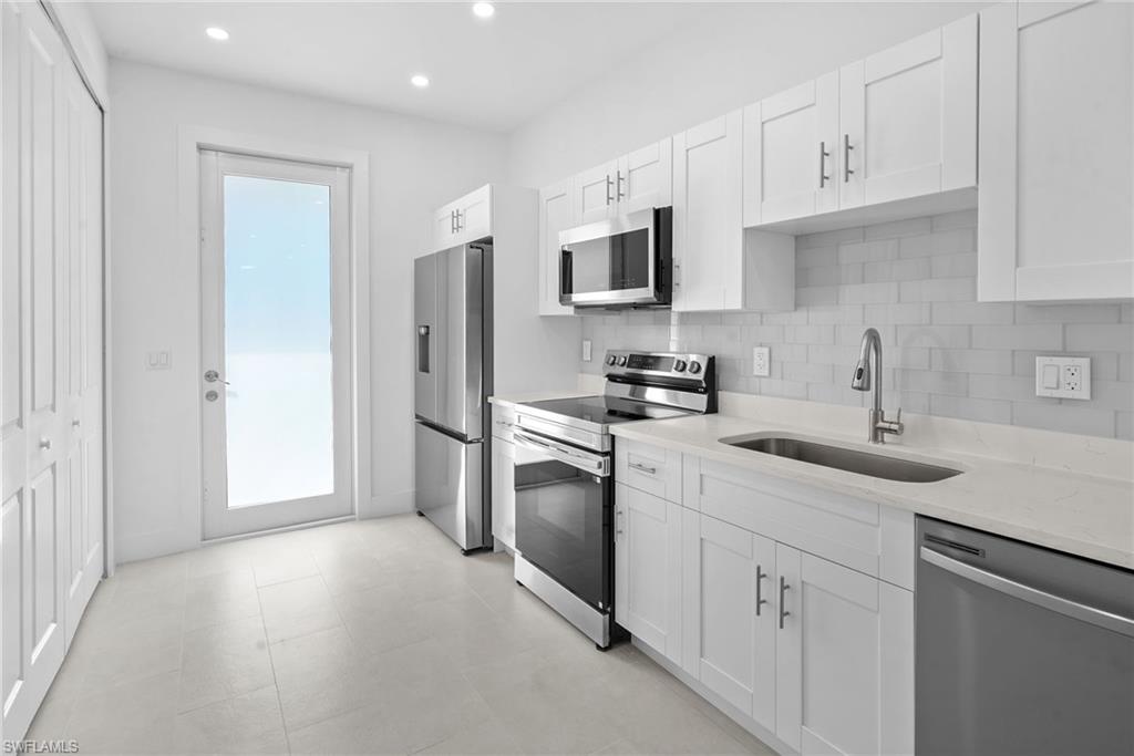 2936 40th Avenue Southeast Naples, FL 34117 - Photo 13 of 49 Kitchen featuring appliances with stainless steel finishes, light stone countertops, decorative backsplash, white cabinetry, and recessed lighting