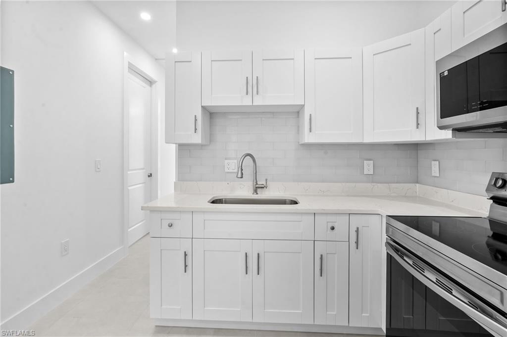 2936 40th Avenue Southeast Naples, FL 34117 - Photo 28 of 49 Kitchen featuring stainless steel appliances, backsplash, white cabinetry, light stone countertops, and recessed lighting