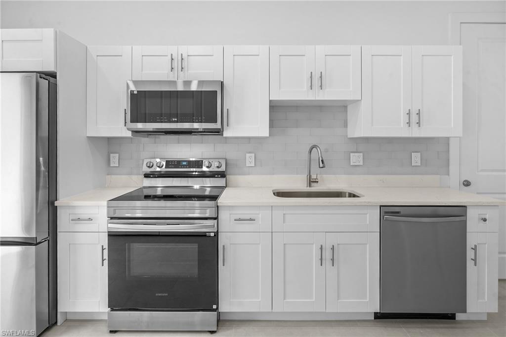 2936 40th Avenue Southeast Naples, FL 34117 - Photo 9 of 49 Kitchen with appliances with stainless steel finishes, decorative backsplash, white cabinets, and light stone counters