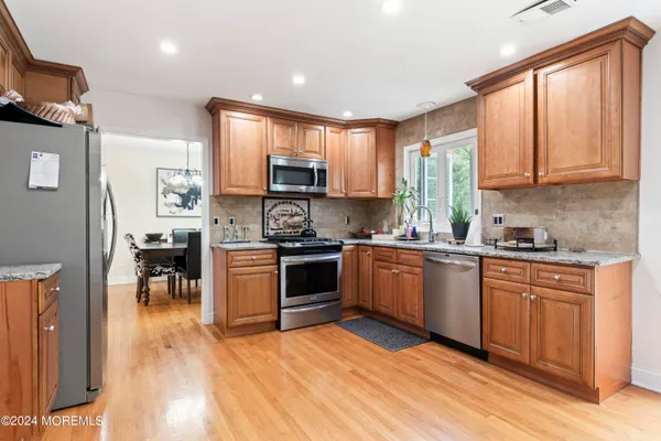 a kitchen with stainless steel appliances granite countertop a stove a sink a refrigerator white cabinets and wooden floor
