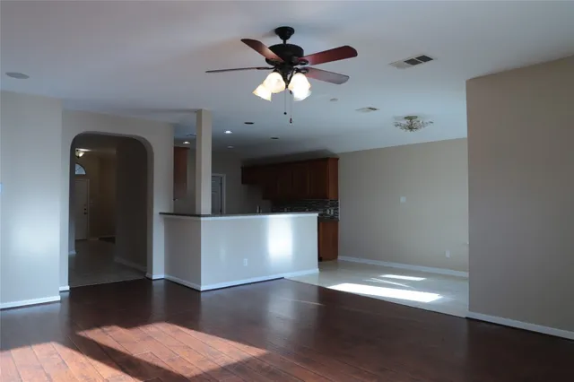 a view of an empty room with wooden floor and a ceiling fan