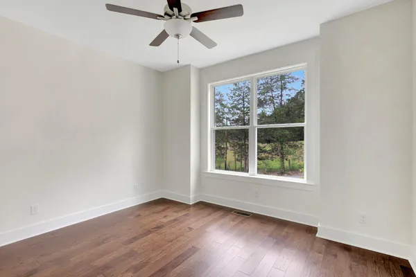 an empty room with wooden floor fan and windows