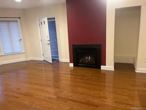 a view of an empty room with wooden floor fireplace and a window