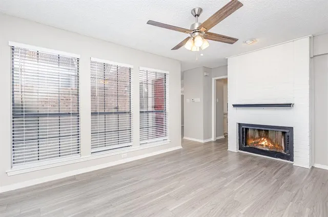 a view of an empty room with wooden floor fireplace and a window