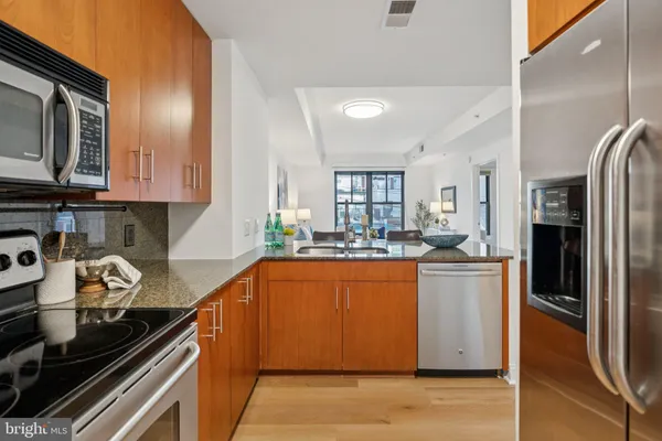 a kitchen with stainless steel appliances granite countertop a refrigerator a stove and a sink with wooden floor