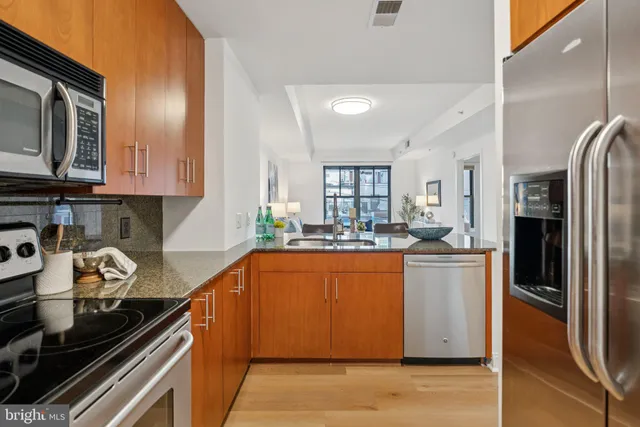 a kitchen with stainless steel appliances granite countertop a refrigerator a stove and a sink with wooden floor