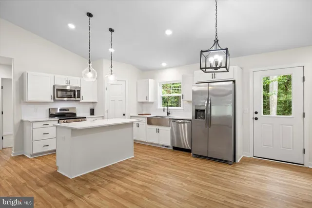 a kitchen with stainless steel appliances kitchen island a refrigerator a sink dishwasher a stove and white cabinets with wooden floor