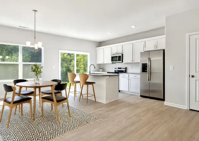 a kitchen with stainless steel appliances granite countertop a stove a refrigerator a kitchen island a dining table and chairs with wooden floor