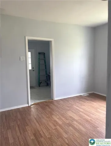 a view of an empty room with wooden floor & a window