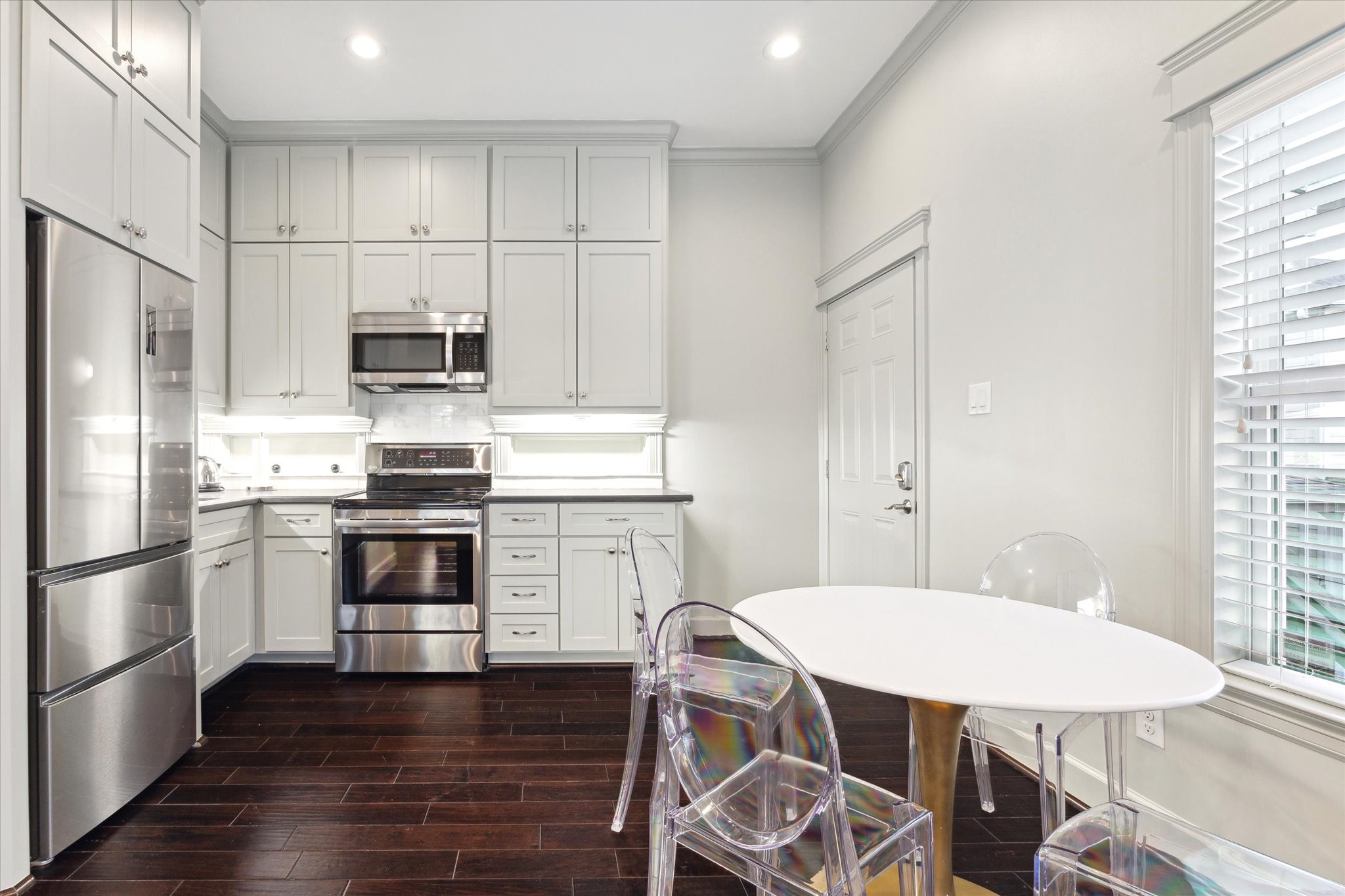 606 Rutland Street Houston, TX 77007 - Photo 39 of 48 The garage apartment kitchen features stainless steel appliances, sleek white cabinetry, and a cozy dining nook.The dark wood floors add warmth and contrast, while ample natural light enhances the space's airy feel.
