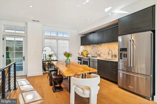 a kitchen with stainless steel appliances a refrigerator a stove a dining table and chairs with wooden floor