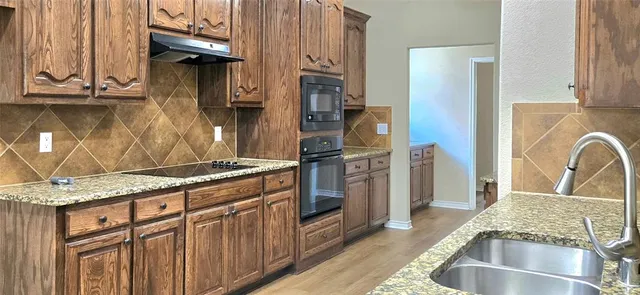 a kitchen with stainless steel appliances granite countertop a refrigerator a stove and a sink with wooden cabinets