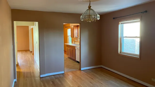 an empty room with wooden floor chandelier and windows