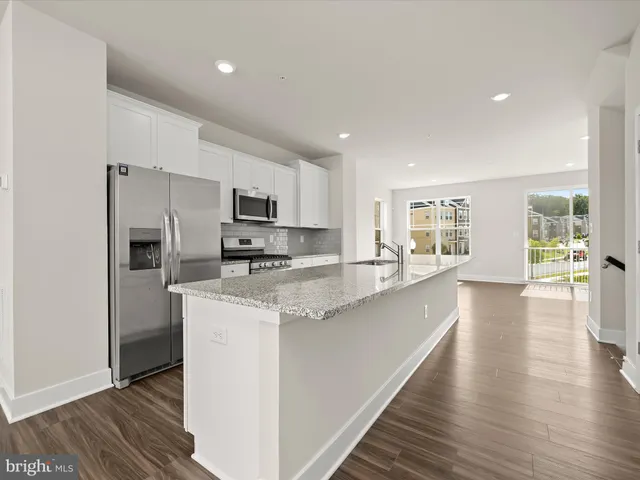 a kitchen with stainless steel appliances a microwave a stove a sink dishwasher a refrigerator and white cabinets with wooden floor