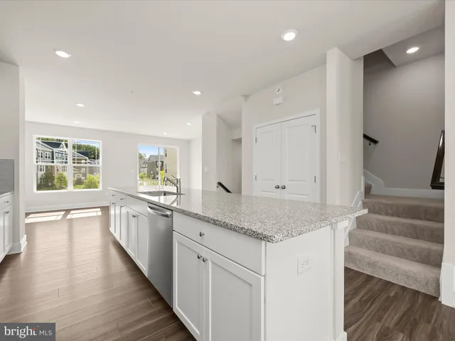 a kitchen with granite countertop a stove a sink and white cabinets with wooden floor