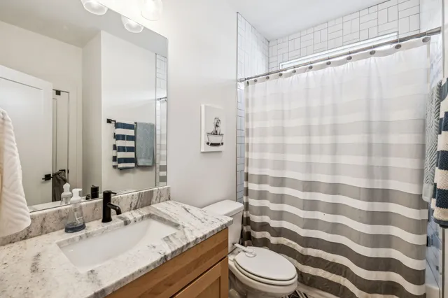 a bathroom with a granite countertop sink a toilet a mirror and shower curtain